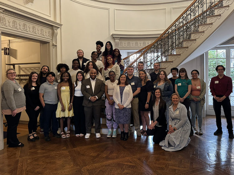 A large group of people in several rows standing near a historic staircase indoors.