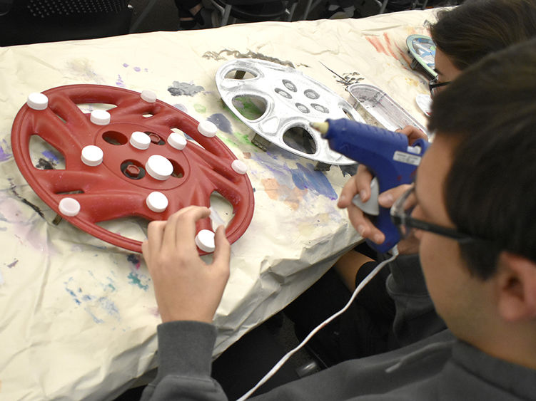 A student paints a hubcup red.
