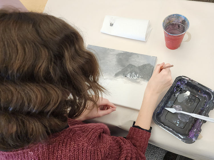 A photo taken behind a student sitting at a table painting.