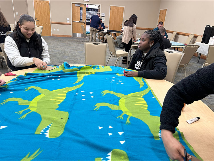 Students work on preparing a blanket laid out on a table.