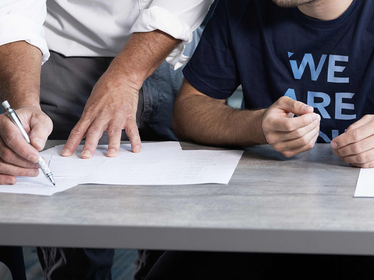 A close-up of the hands of an instructor writing on a sheet of paper next to the hands of a student seated alongside.