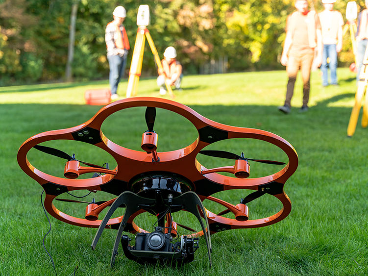 A drone on the grass with surveying equipment and people in the background.