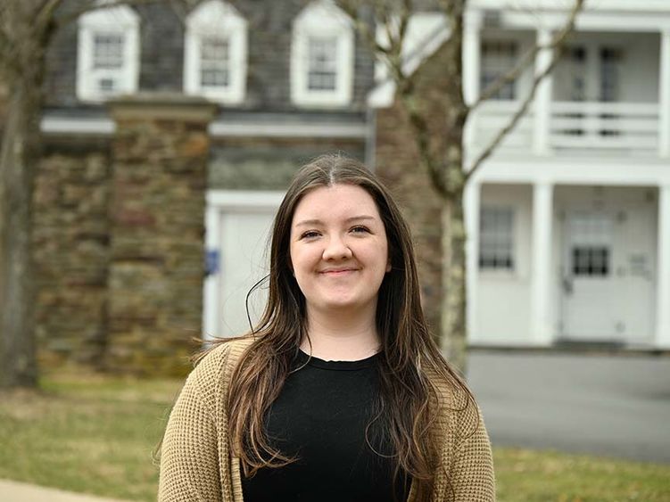 A female student stands outside in front of historic Hayfield House.